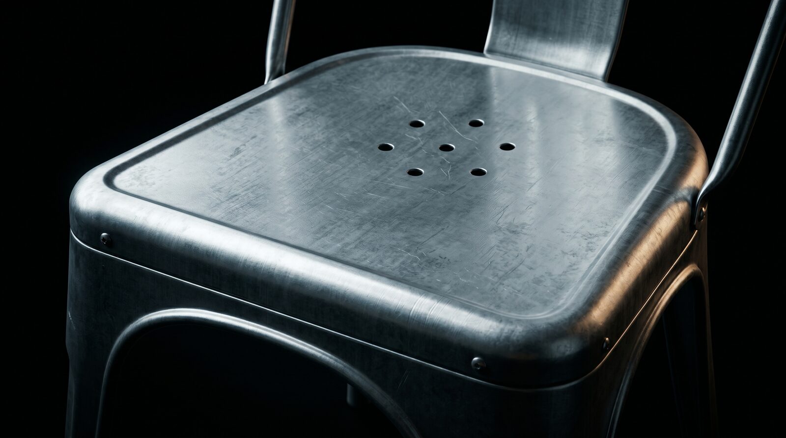 Macro photograph of the Tolix Model A's pressed steel seat plate, showing the rolled lip and ventilation holes.